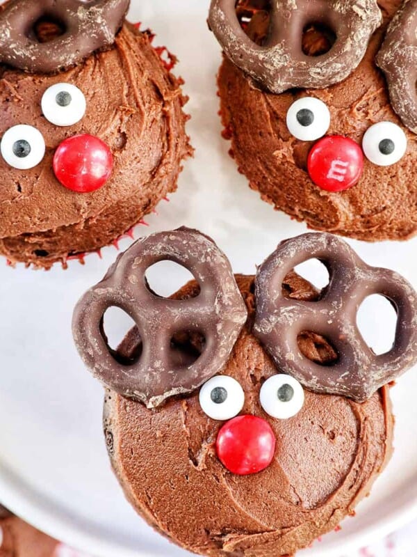 three reindeer cupcakes with chocolate buttercream frosting on a plate.