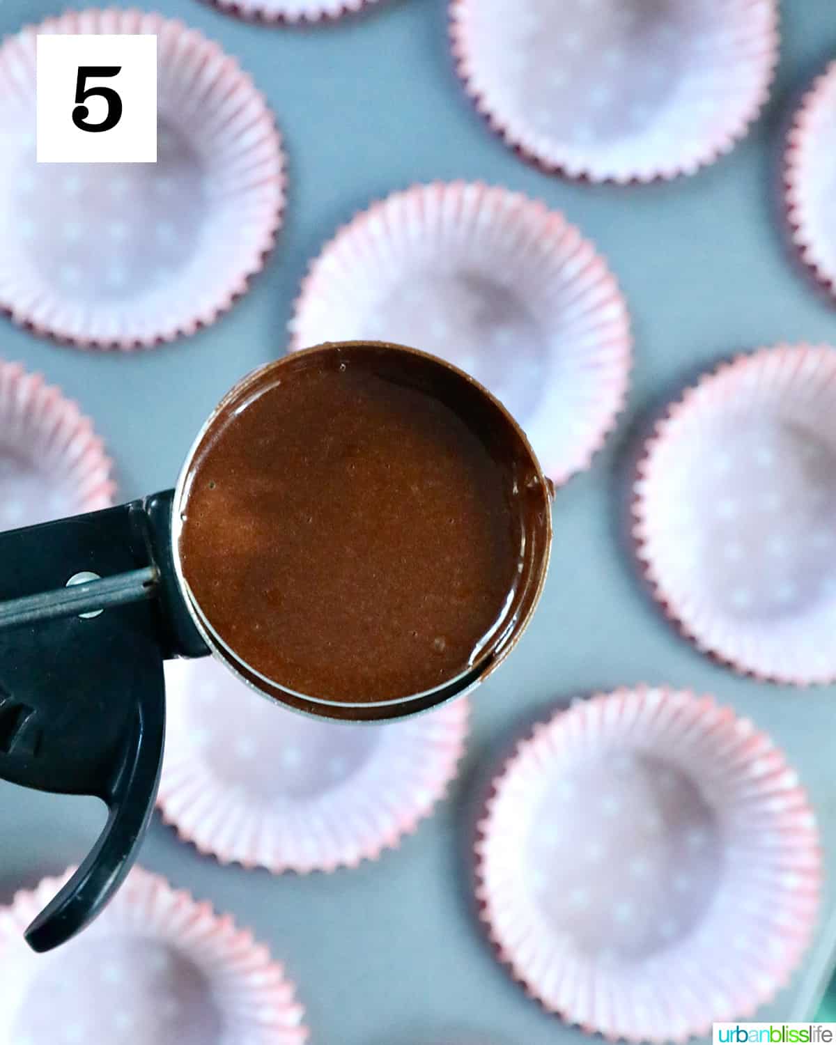 cookie scoop full of chocolate cupcake batter over a muffin tin.