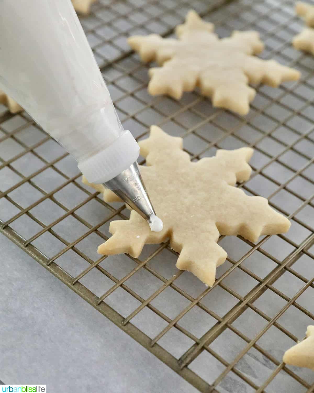 royal icing piping onto a snowflake sugar cookie on a wire rack.