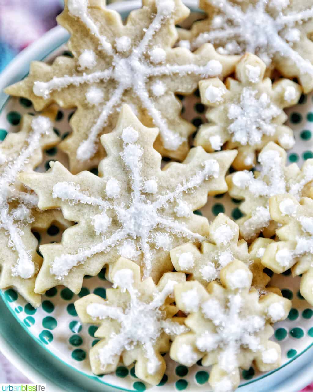 plate full of snowflake sugar cookies decorated with royal icing and decorator sugar.