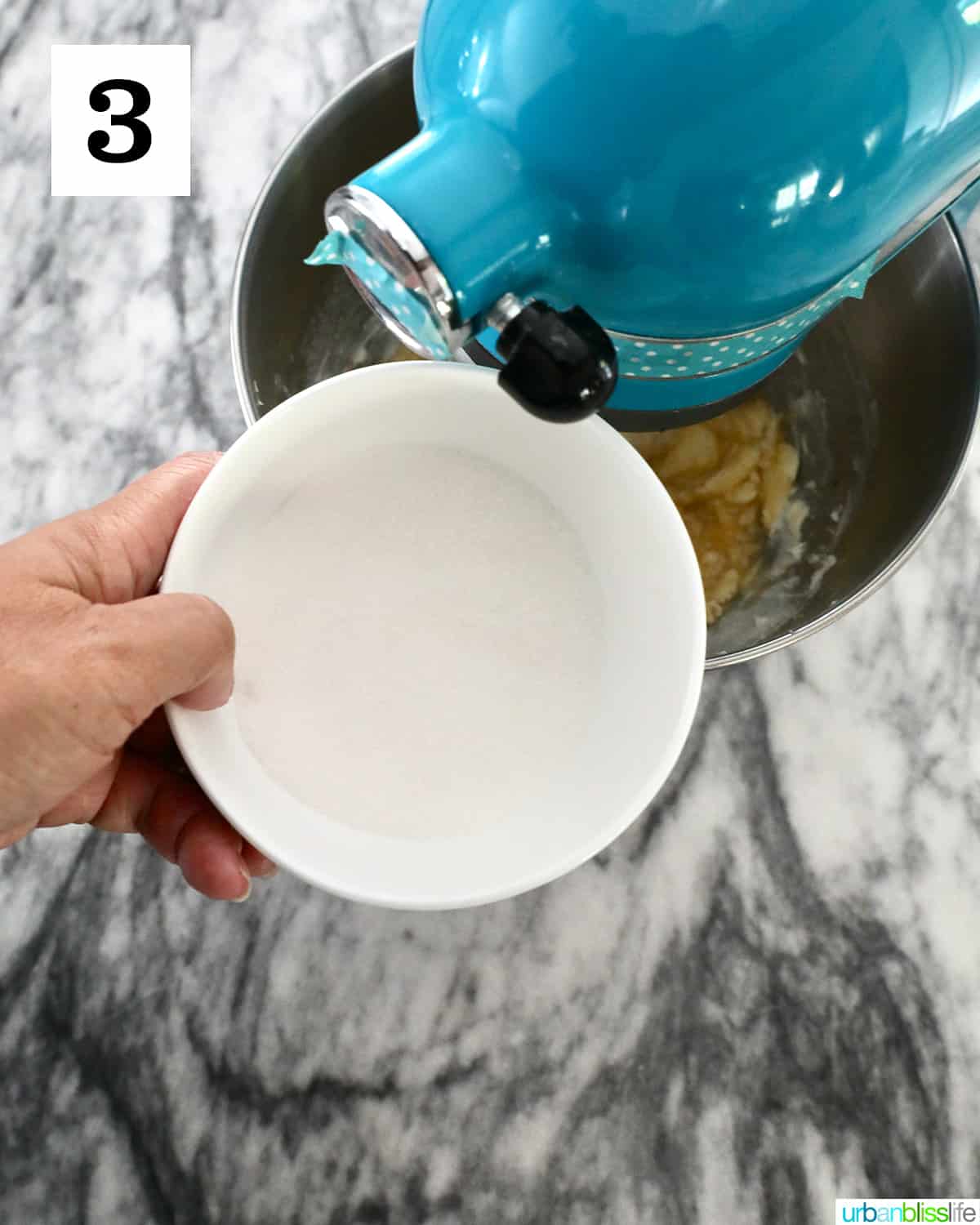 adding sugar to cookie batter in a blue stand mixer.