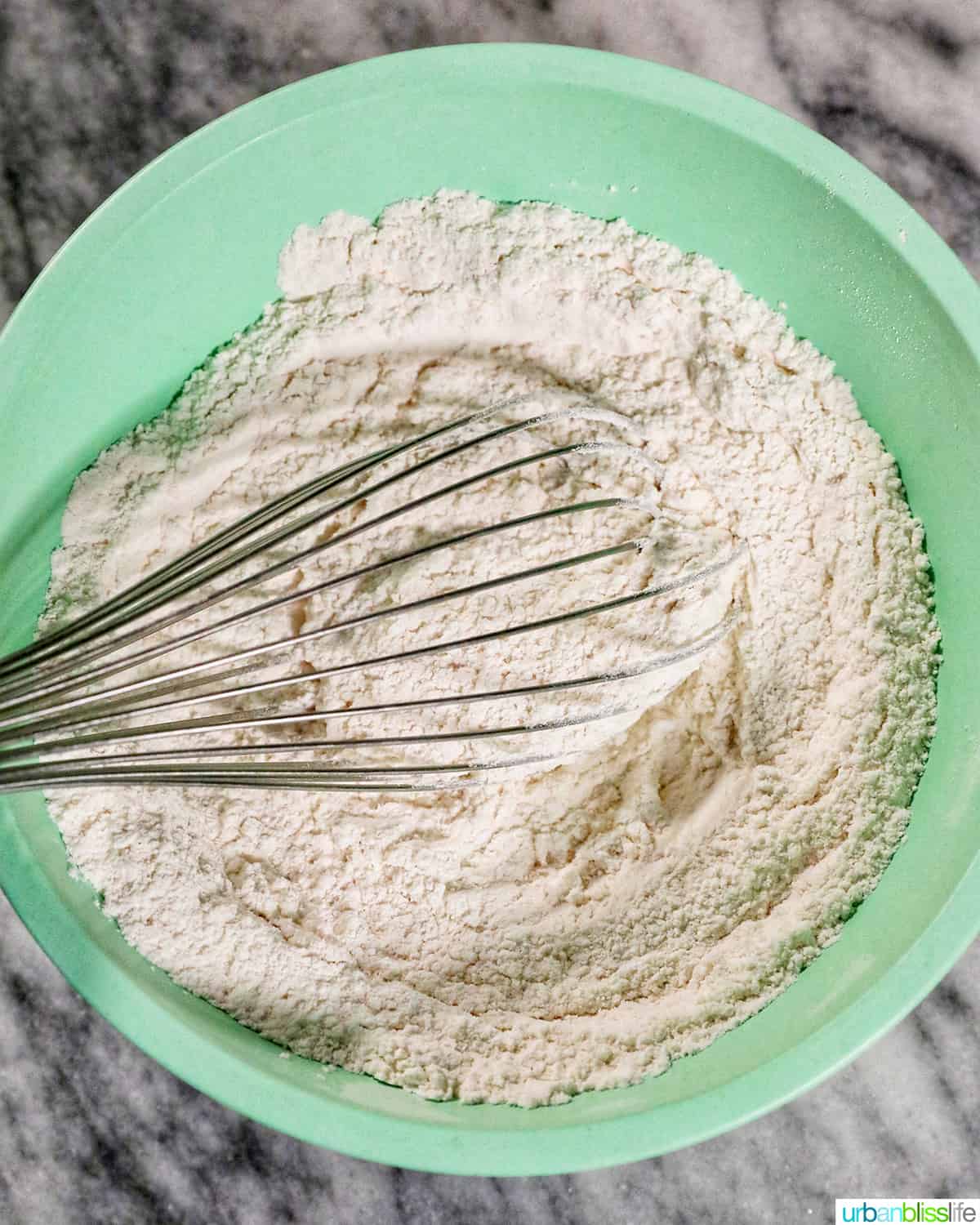 whisk with dry baking ingredients in a green bowl.