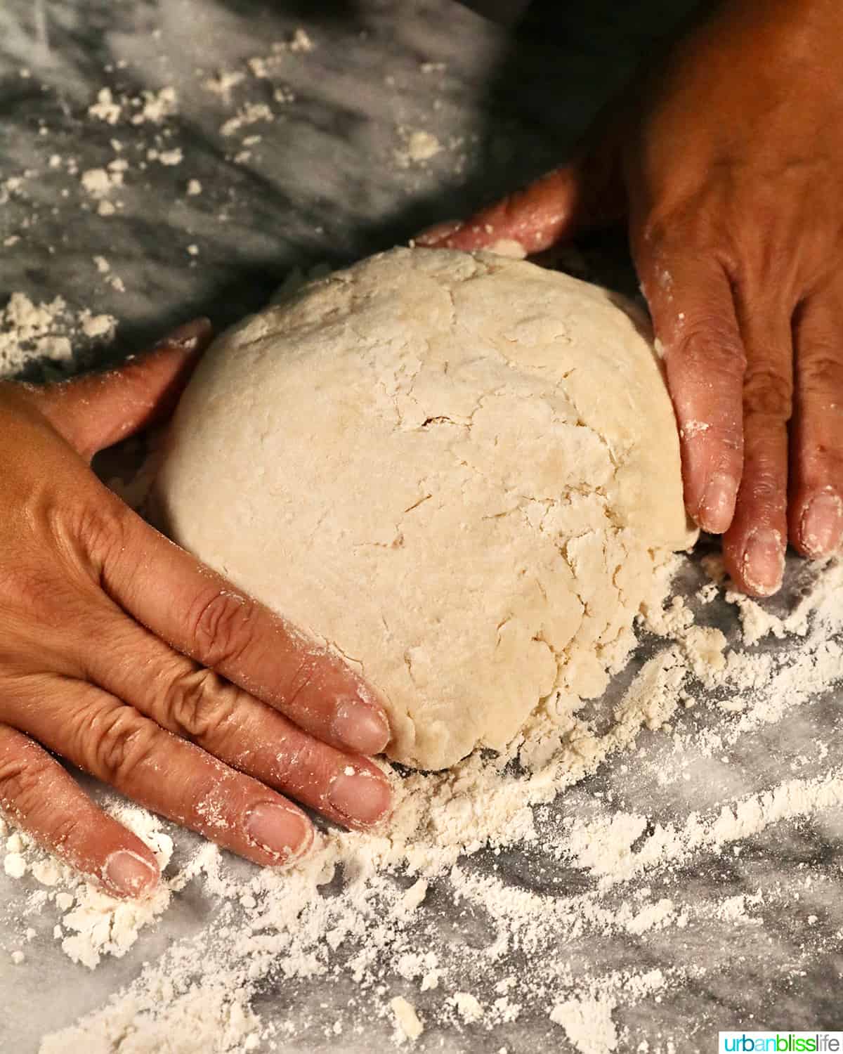 hands shaping biscuit dough on a marble countertop.