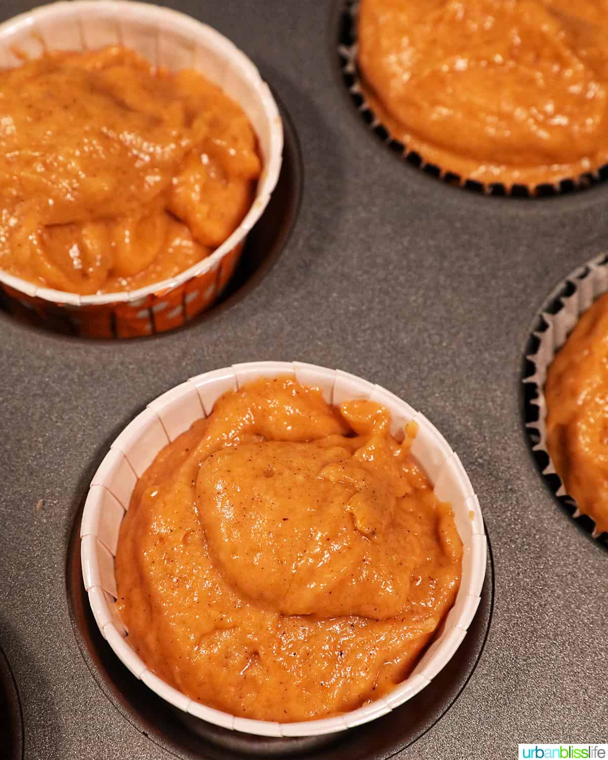 muffin cups filled with orange pumpkin banana muffin batter in a muffin tin.