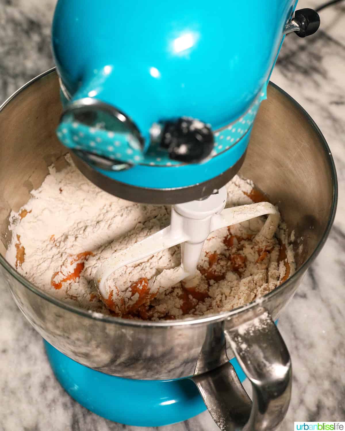 blue stand mixer with flour and ingredients mixing to make pumpkin banana muffins.
