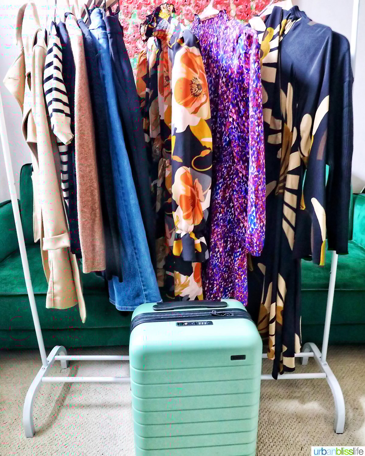 clothing rack with clothes hung up and a green away suitcase.
