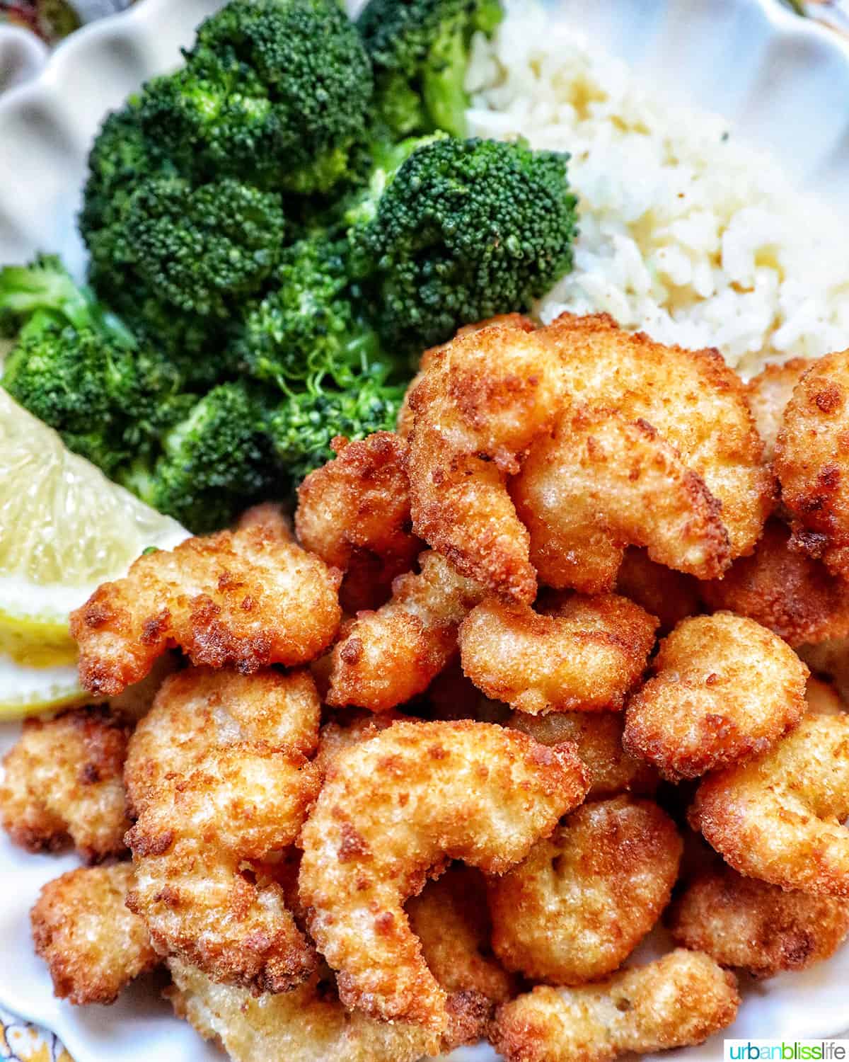 airfryer popcorn shrimp on a plate with broccoli, lemon wedges.