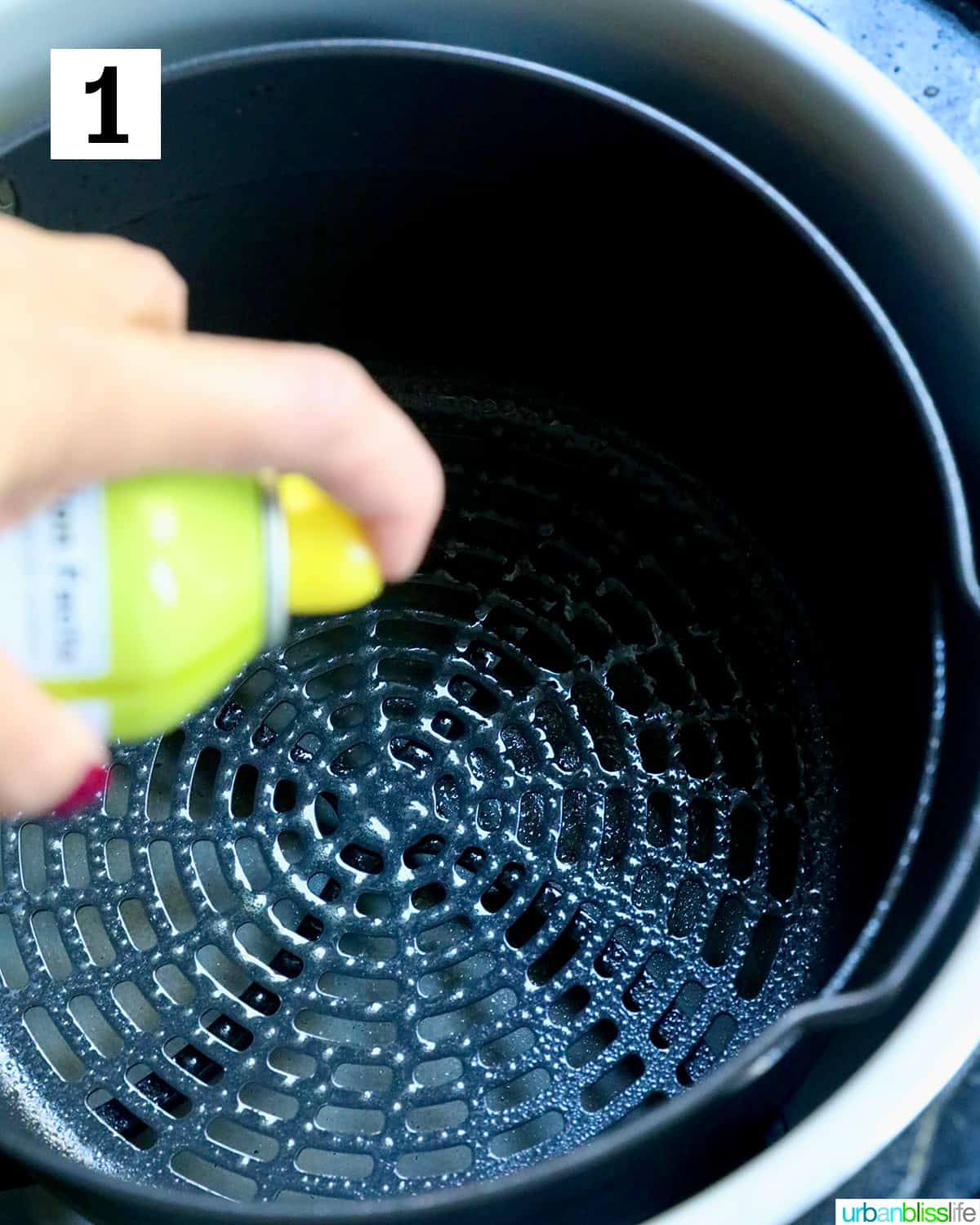spraying air fryer basket with olive oil spray.