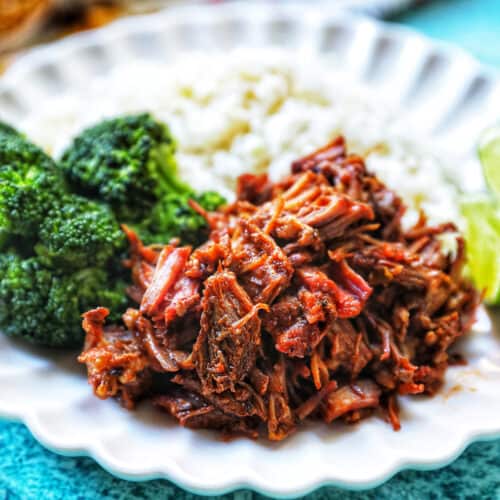 Mexican shredded beef on a plate with rice and broccoli.