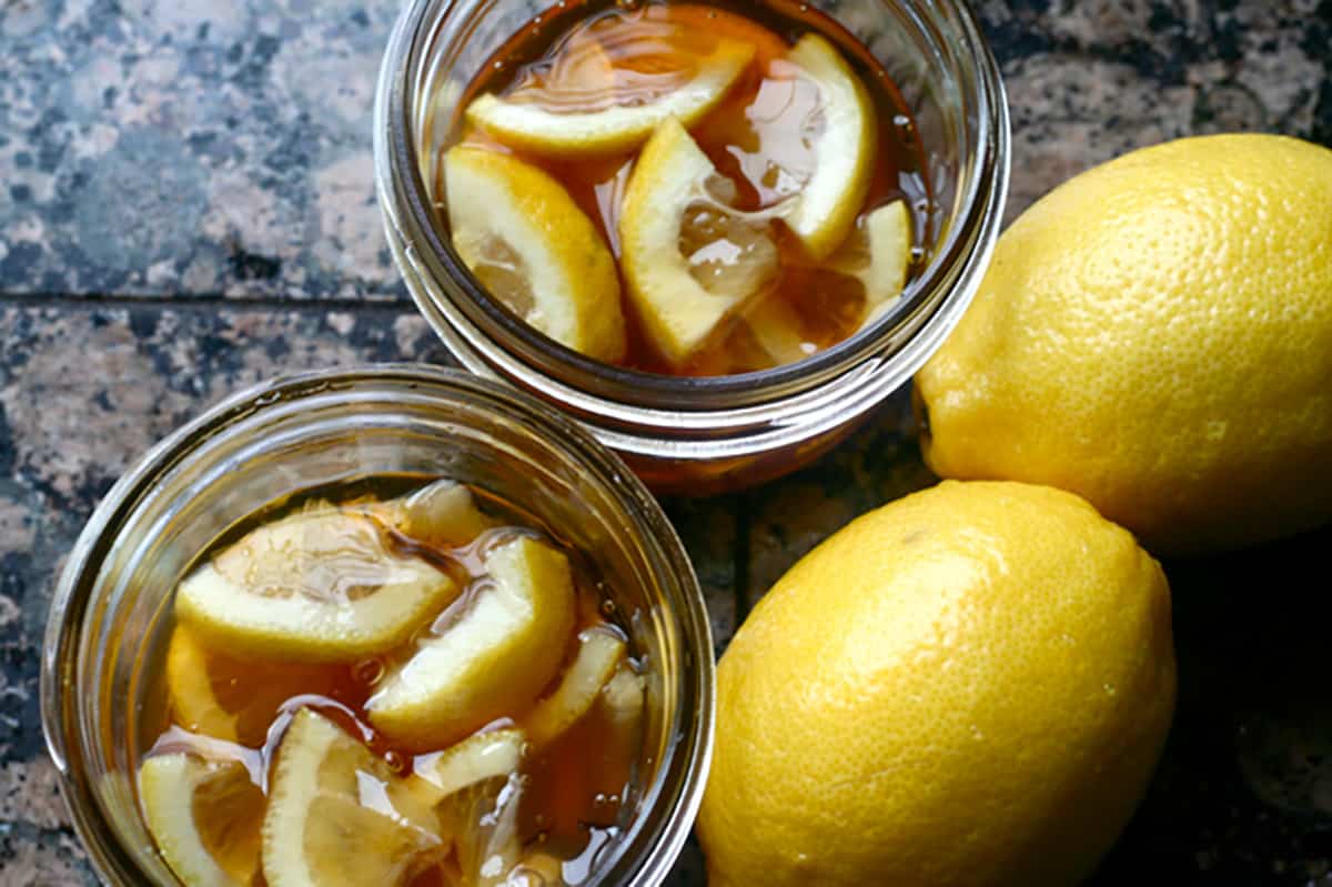 two mason jars of ginger lemon and honey marmalade, with two lemons on the side