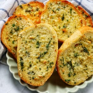 plate full of sliced garlic bread with kitchen towel.