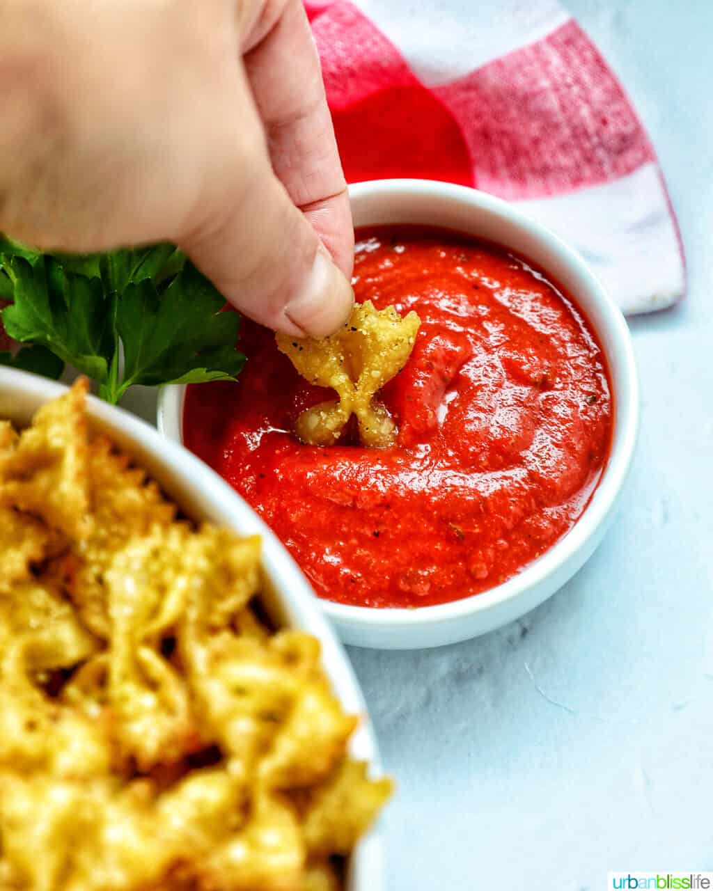 hand dipping a pasta chip into marinara sauce.