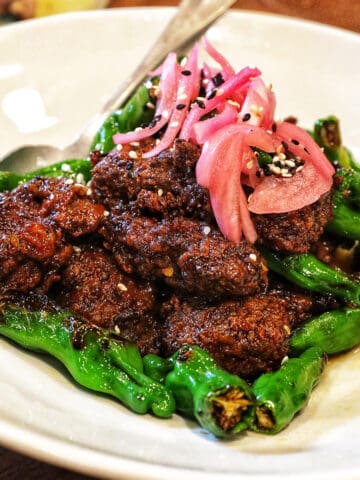 ginger beef with pickled onions and shishito peppers on a white plate.