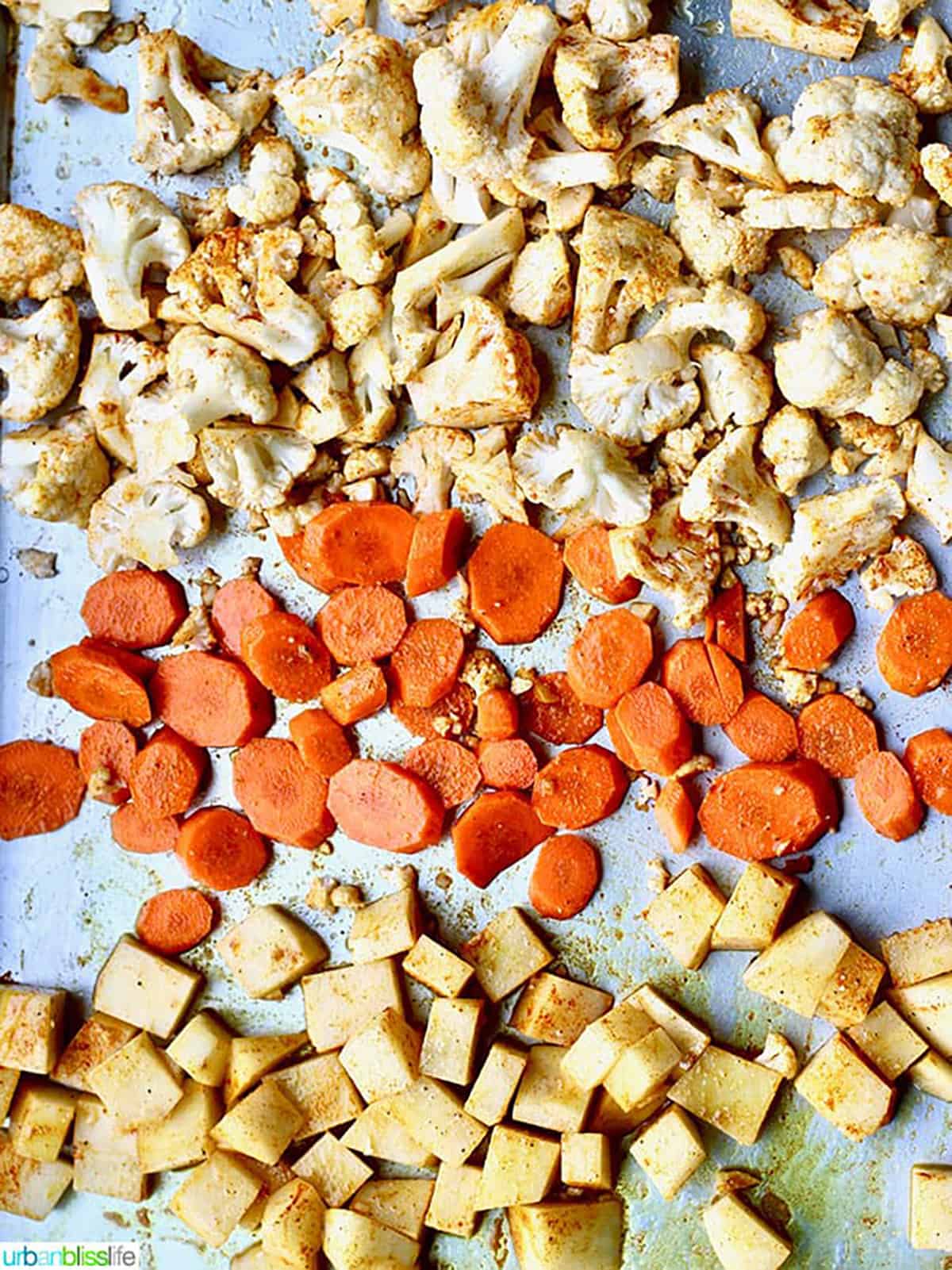 sheet pan filled with chopped and seasoned cauliflower, carrots, potatoes.
