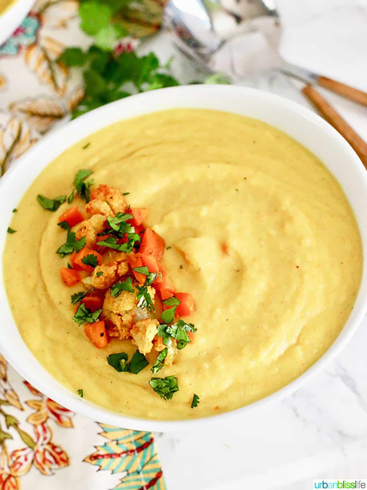 white bowl filled with Cauliflower Carrot Soup and topped with chopped cauliflower, carrots and parsley.