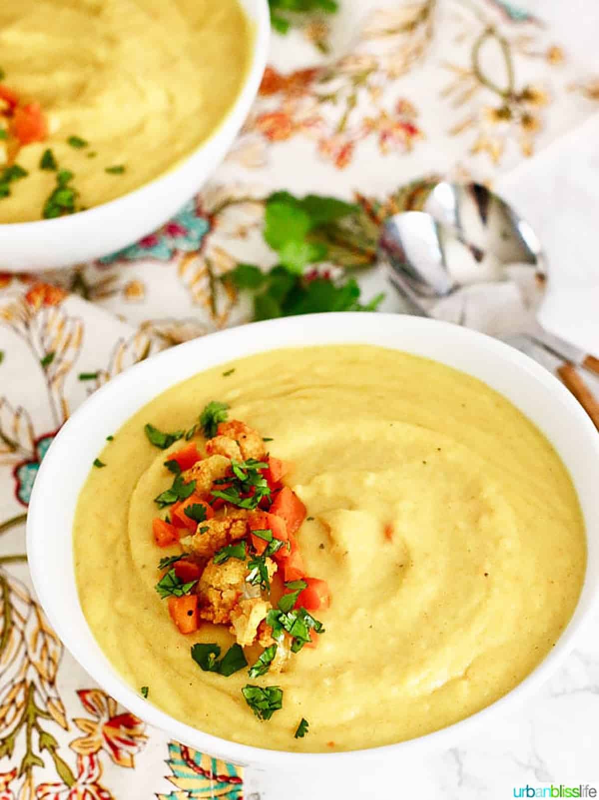 white bowl filled with Cauliflower Carrot Soup and topped with chopped cauliflower, carrots and parsley.