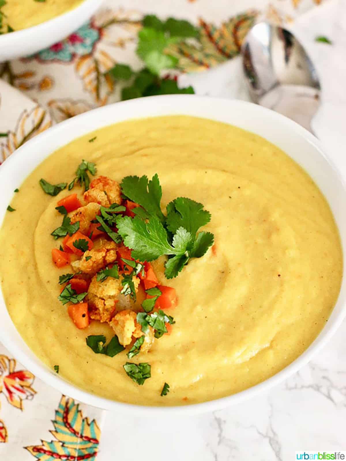 Cauliflower Carrot Soup in white bowl and with chopped cauliflower, carrots and parsley.