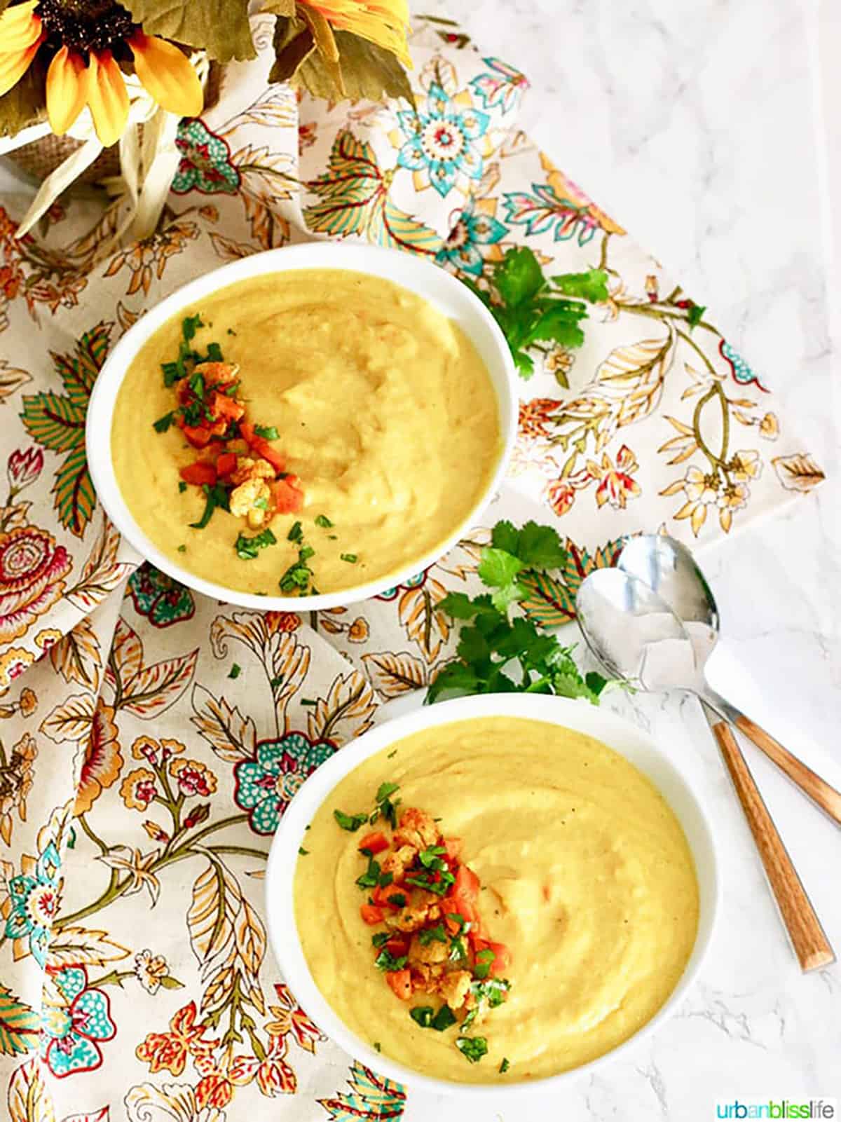 Two white bowls filled with Cauliflower Carrot Soup and topped with chopped cauliflower, carrots and parsley.