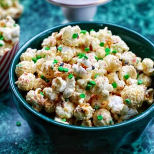 Christmas popcorn mix in a green bowl on a green table.