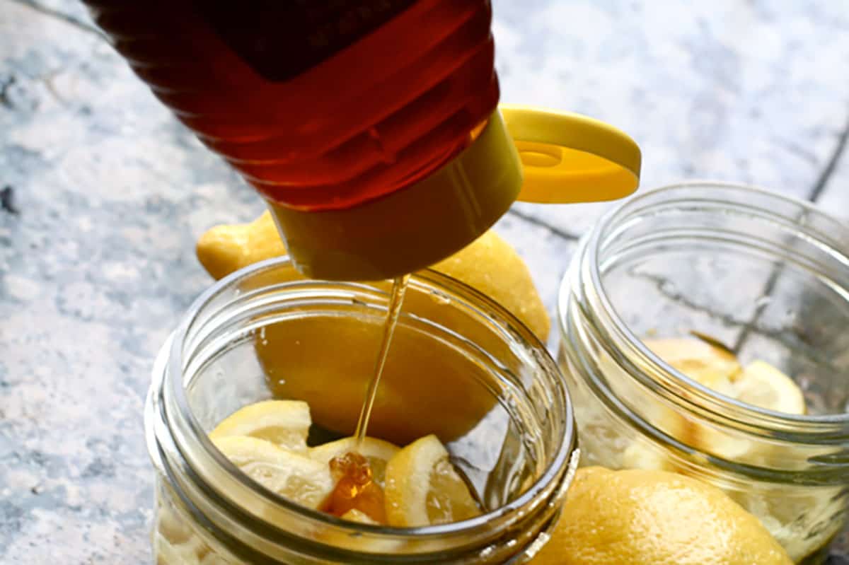 pouring honey into a mason jar containing lemon wedges