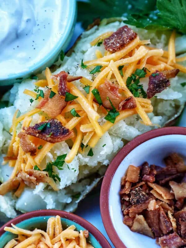 Loaded air fryer baked potato with title text overlay and sides of sour cream, cheddar cheese, parsley, and bacon.