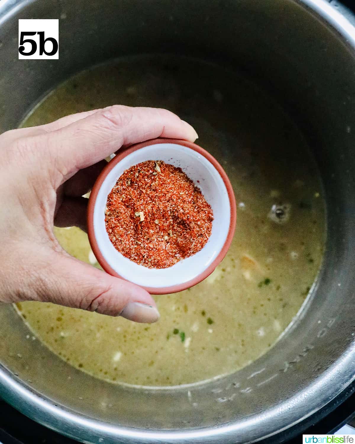 hand holding a small bowl of Cajun seasoning being added to the Instant Pot.