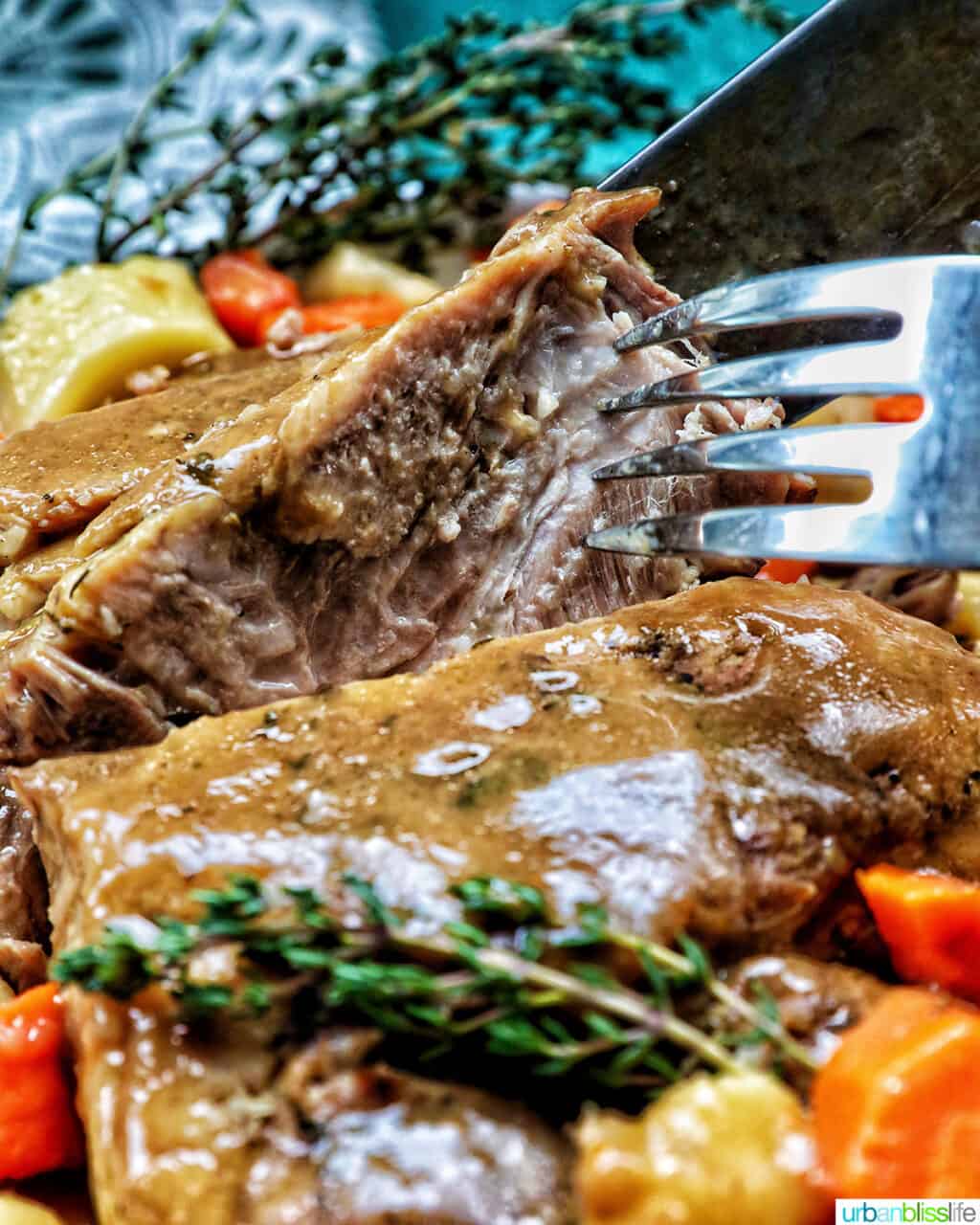 fork and knife holding up a slice of Instant Pot pork roast with potatoes, carrots and herbs.
