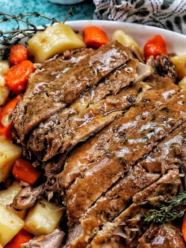 sliced pork roast with chopped carrot and potatoes on it, topped with gravy and herbs.