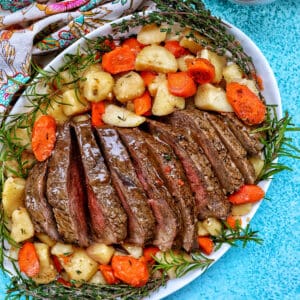 Sliced sirloin tip roast surrounded by carrots, potatoes, and herbs with a side of gravy.