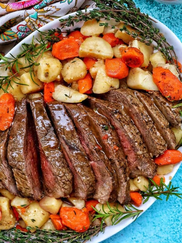 Sliced sirloin tip roast surrounded by carrots, potatoes, and herbs with a side of gravy.