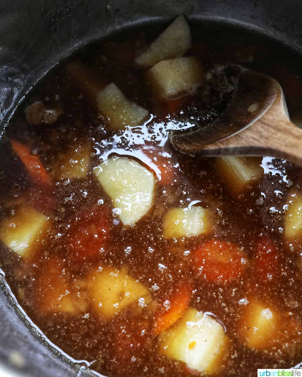 wooden spoon stirring potatoes and carrots in beef broth in an Instant Pot electric pressure cooker.