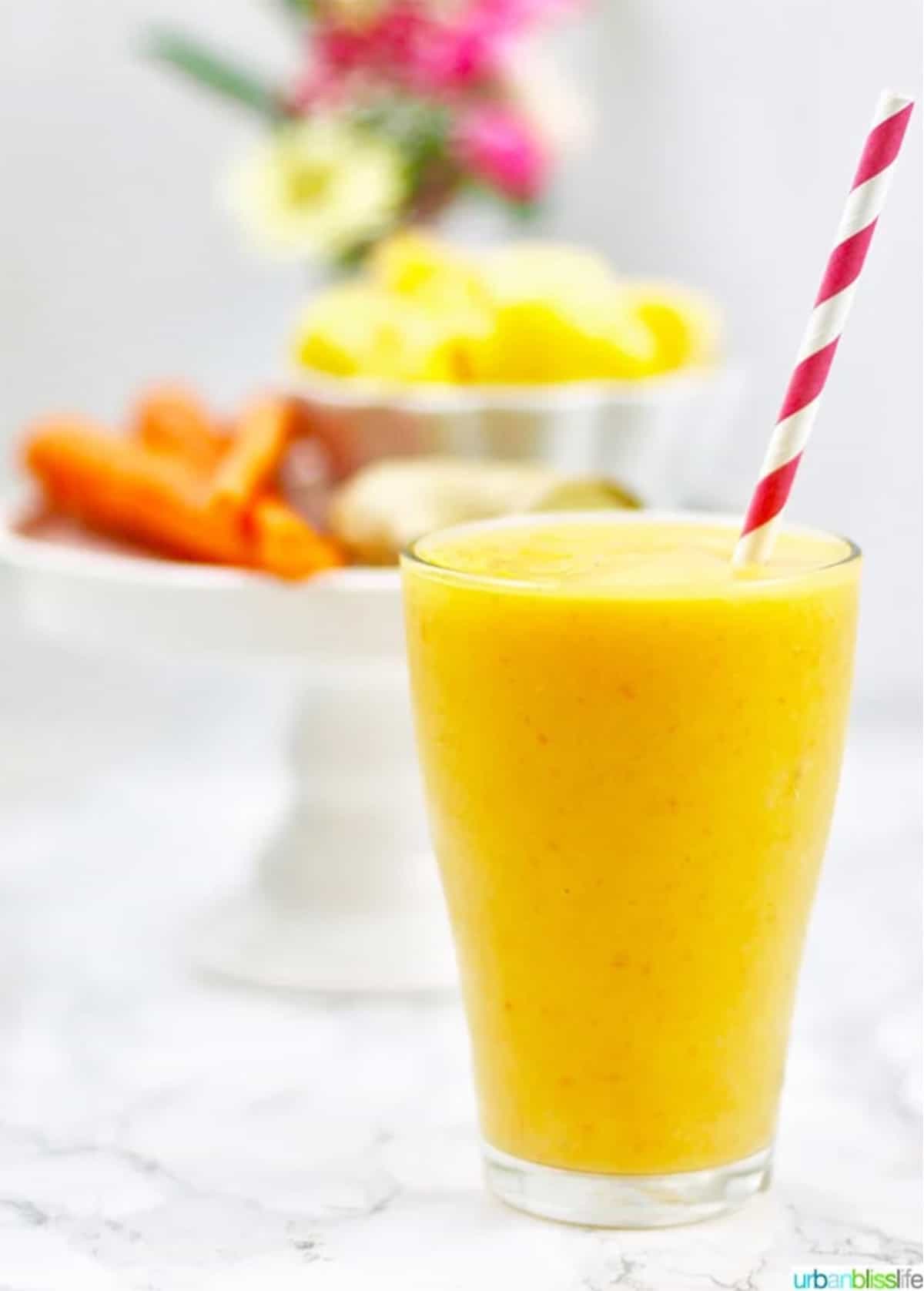 mango carrot smoothie in glass with red and white straw