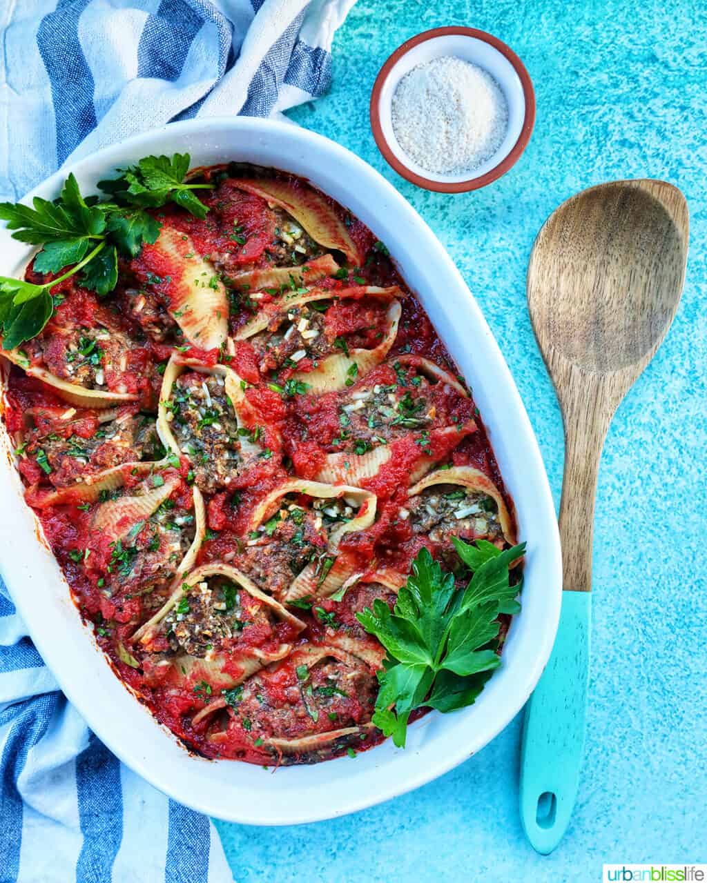 casserole dish of stuffed shells with ground beef with a wooden spoon and side of dairy free parmesan cheese.