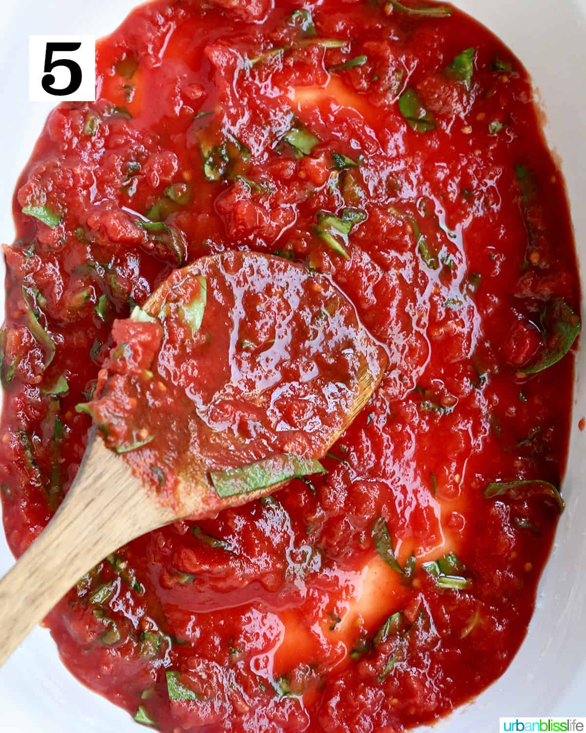 wooden spoon placing a layer of marinara sauce in a casserole dish.