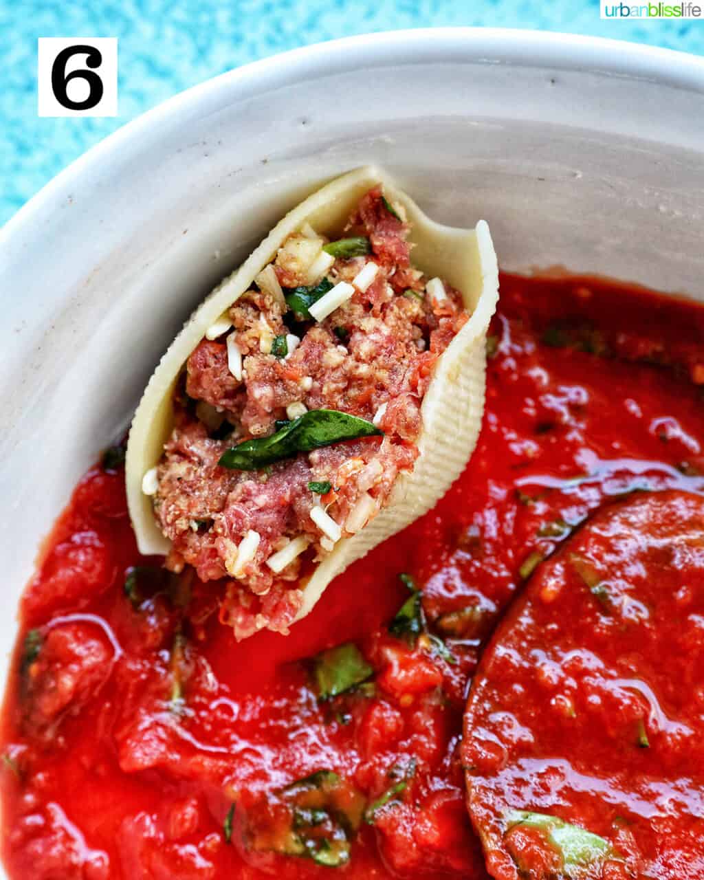 one uncooked stuffed shell with ground beef placed in a casserole dish on top of marinara sauce.
