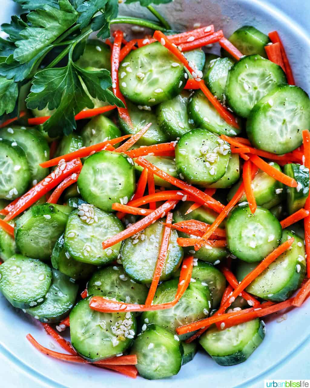 salad bowl full of sliced cucumbers, carrots, and sesame seeds.