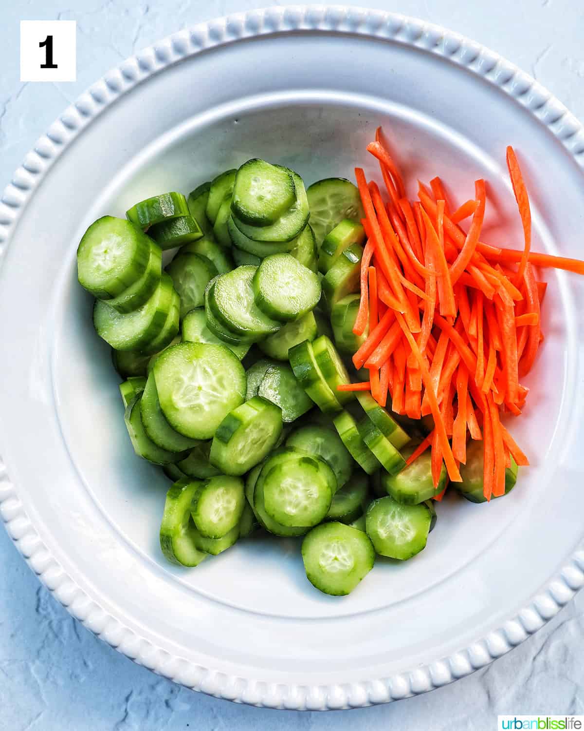 large white bowl with sliced cucumbers and carrots.