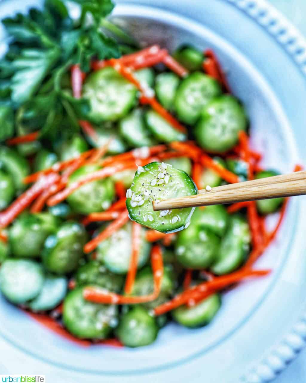 chopsticks holding up a cucumber slice over Asian Carrot Cucumber Salad.