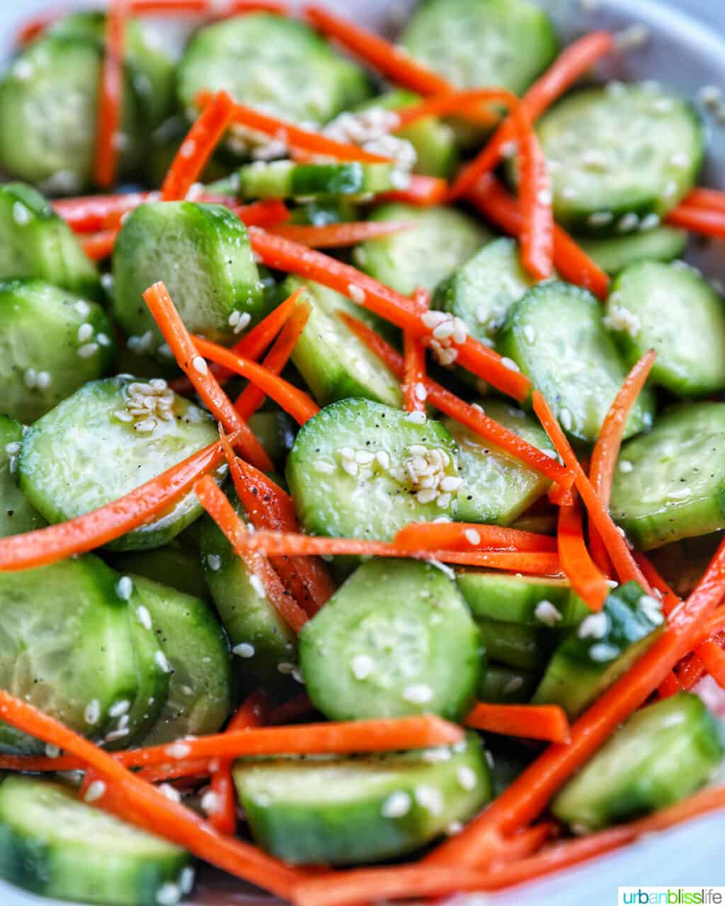 salad bowl full of sliced cucumbers, carrots, and sesame seeds.