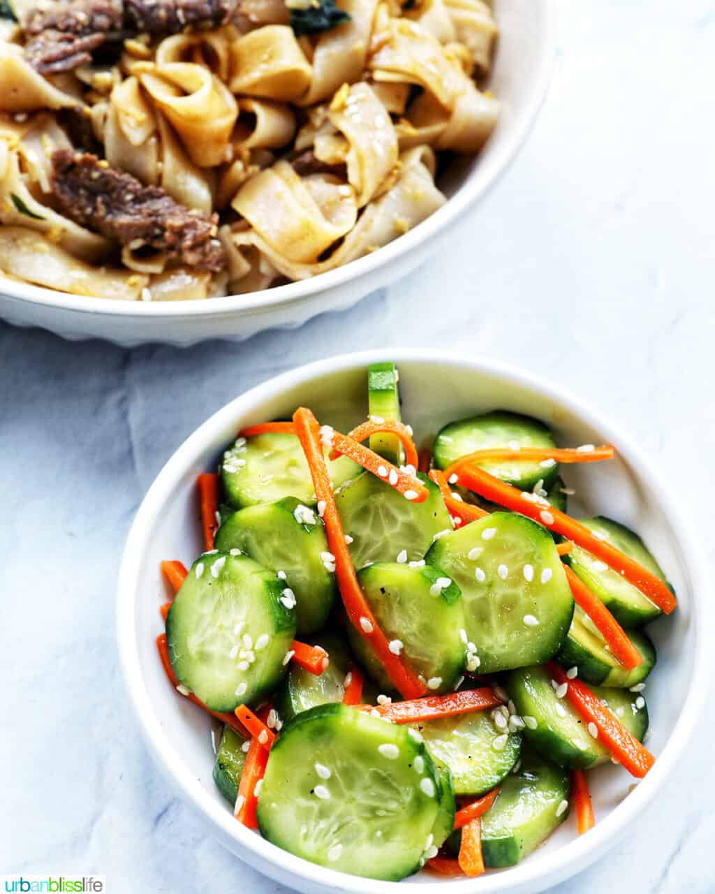 salad bowl full of sliced cucumbers, carrots, and sesame seeds with side of Beef Pad See Ew.