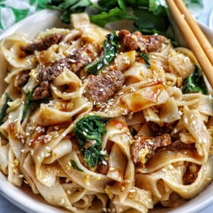 bowl of beef pad see ew noodles, bok choy, chopsticks.