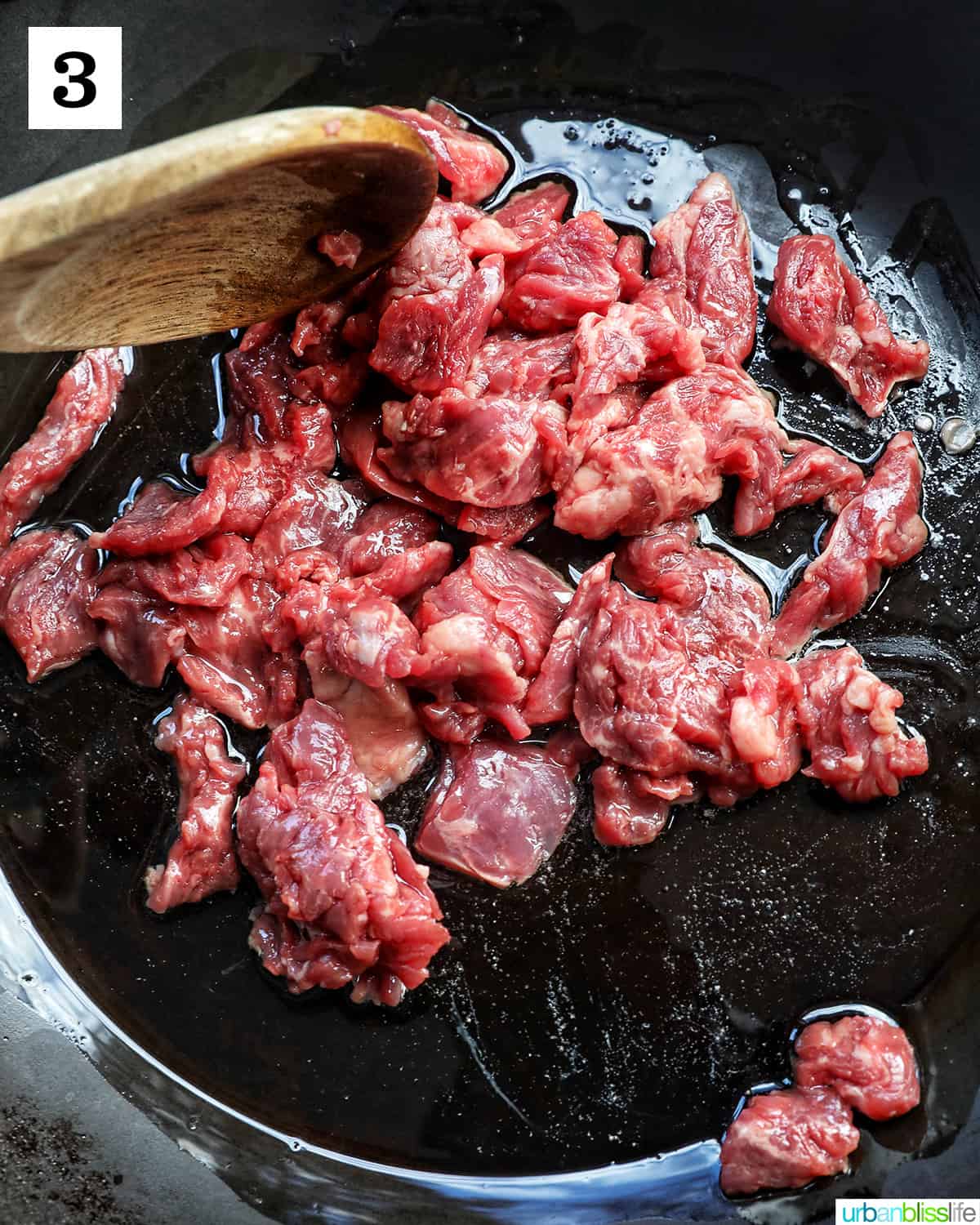 sliced steak cooking in a wok with a wooden spoon stirring.