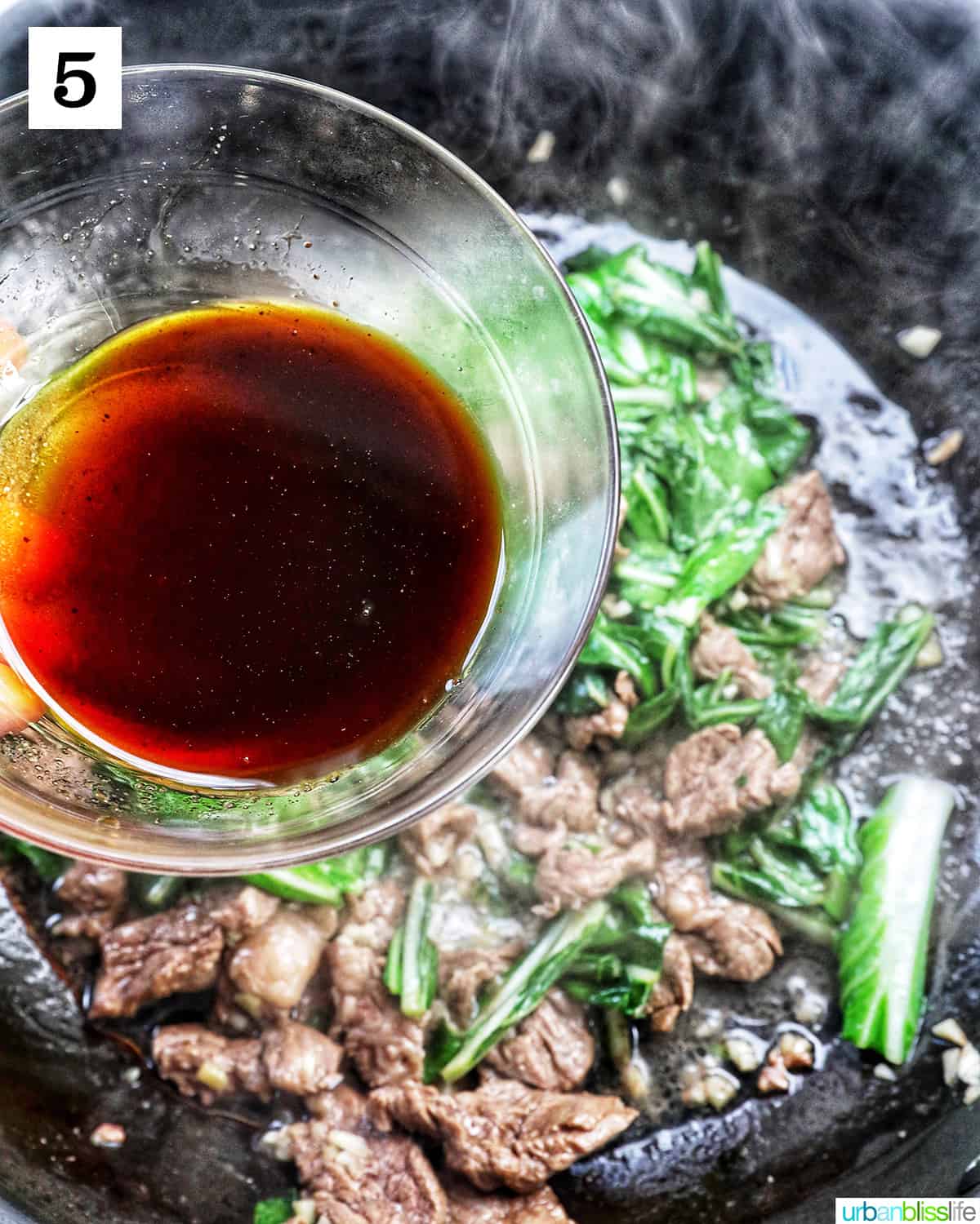 bowl of sauce over a wok of beef and bok choy.