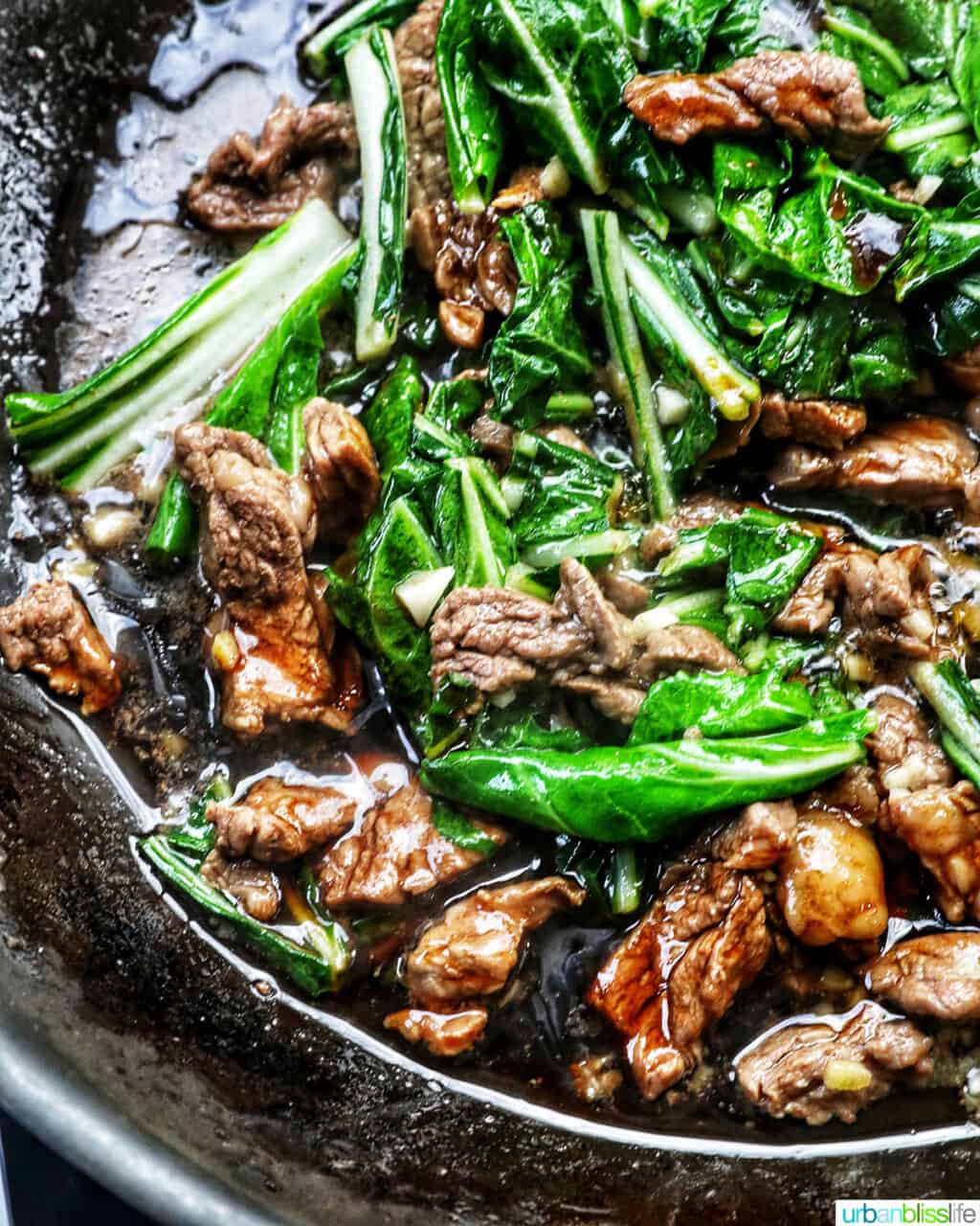 beef and bok choy cooking in a wok.
