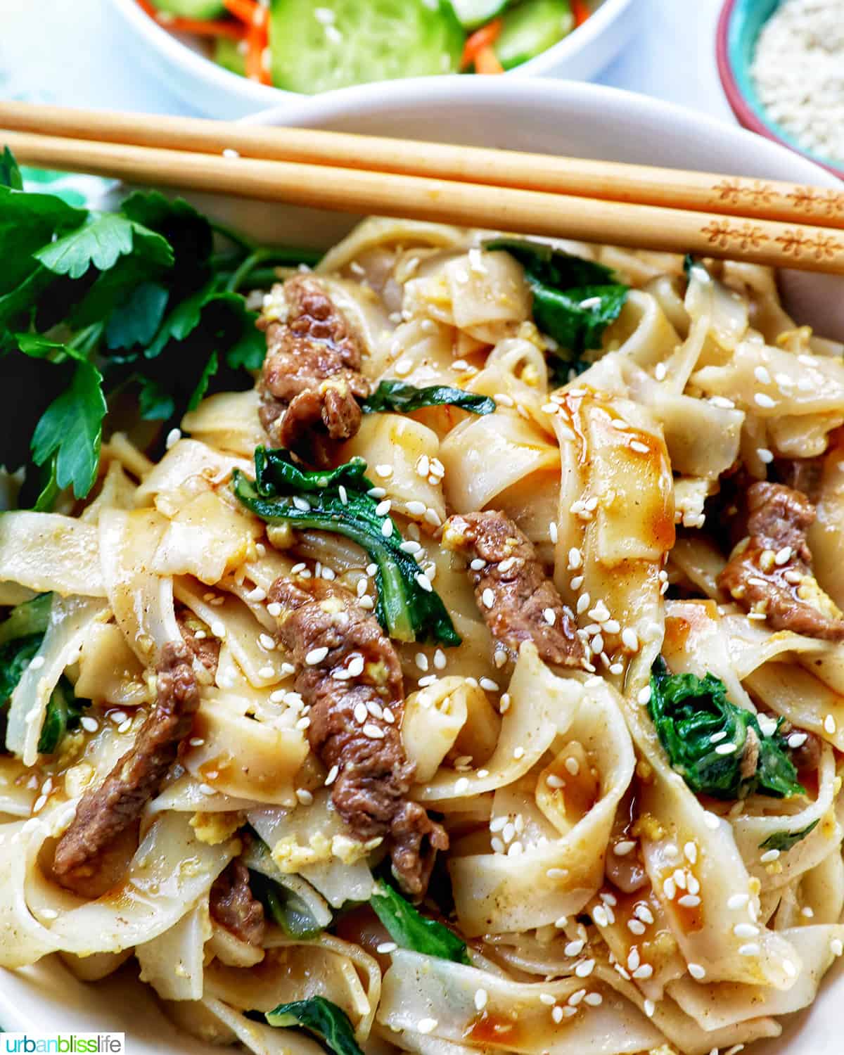 bowl of beef pad see ew noodles, bok choy, chopsticks.