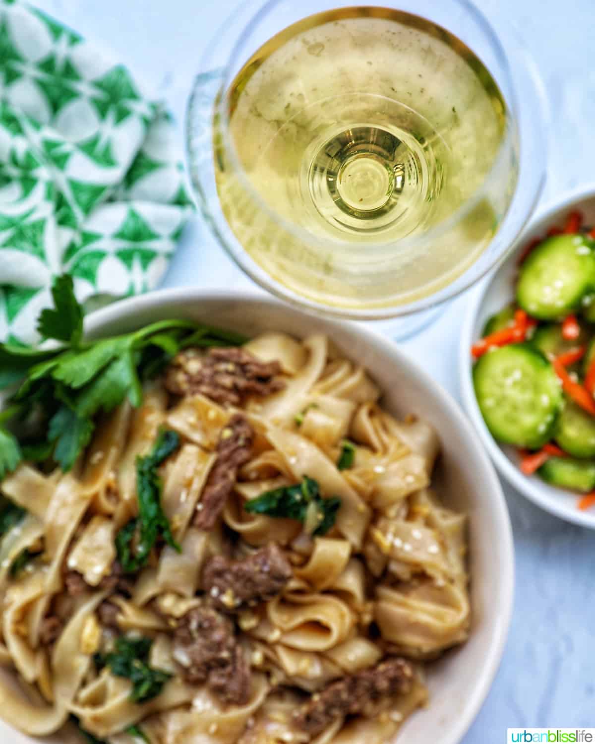 bowl of beef pad see ew noodles, bok choy with side of white wine and cucumber salad.