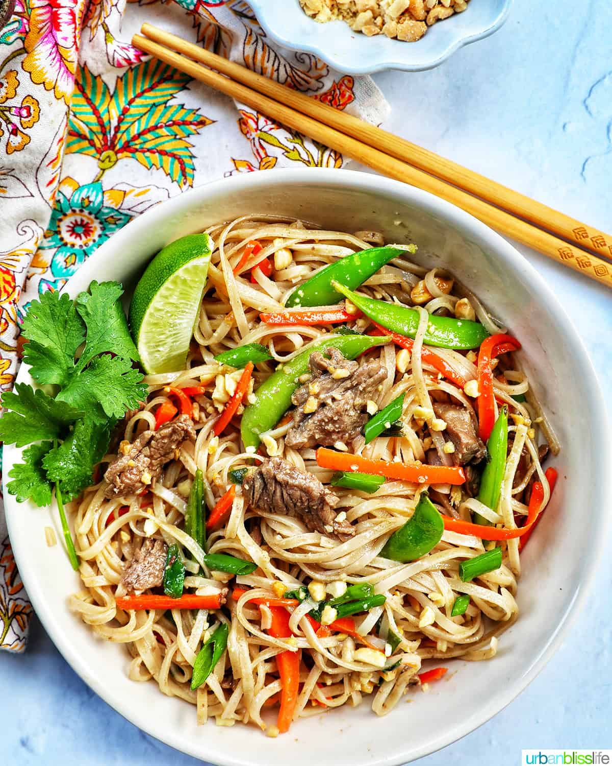 beef pad thai noodles in a white bowl with chopsticks above.