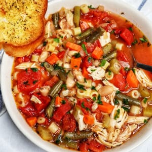 Chicken Minestrone Soup in a white bowl with side of garlic bread.