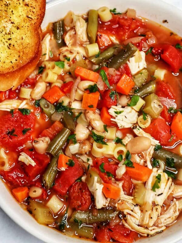 Chicken Minestrone Soup in a white bowl with side of garlic bread.