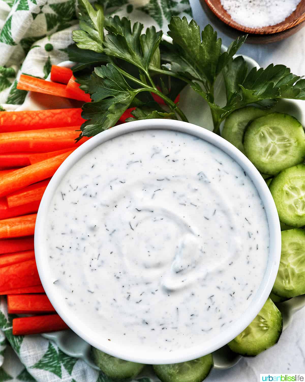 bowl of dairy free ranch dressing with carrot sticks, cucumber slices, and herbs.